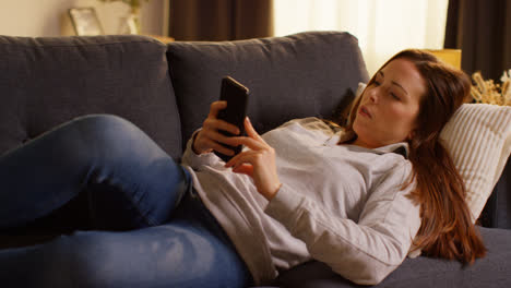 Primer-Plano-De-Una-Mujer-Tumbada-En-Un-Sofá-En-Casa-Viendo-Una-Película-O-Viendo-Una-Película-O-Navegando-Por-Internet-En-Un-Teléfono-Móvil-1